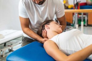 Pregnant woman using a wrapped heating pad on her lower back while seated with pillows for support.