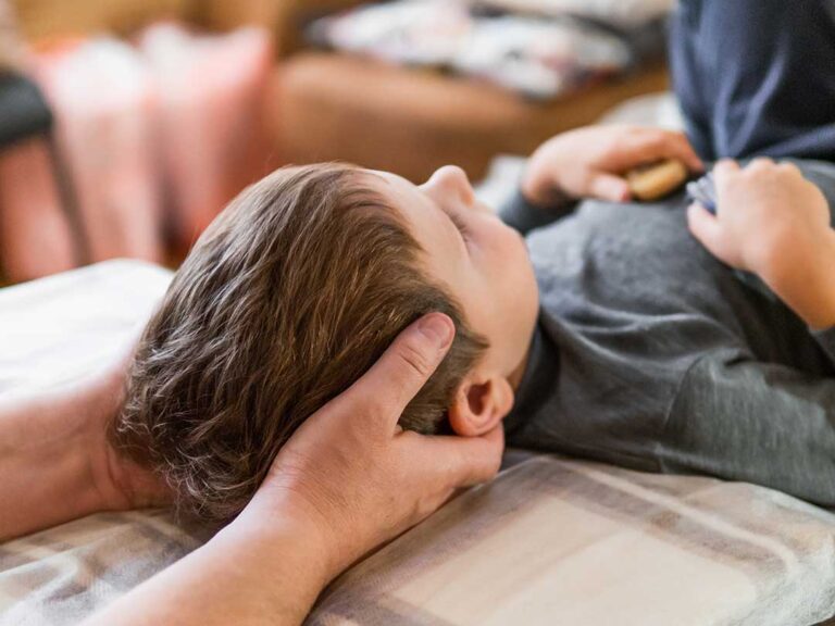 A chiropractor assessing a young athlete’s posture on a gym mat with sports equipment nearby.