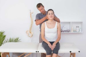 Person examining a painful foot while standing beside a simple spine and leg alignment diagram.